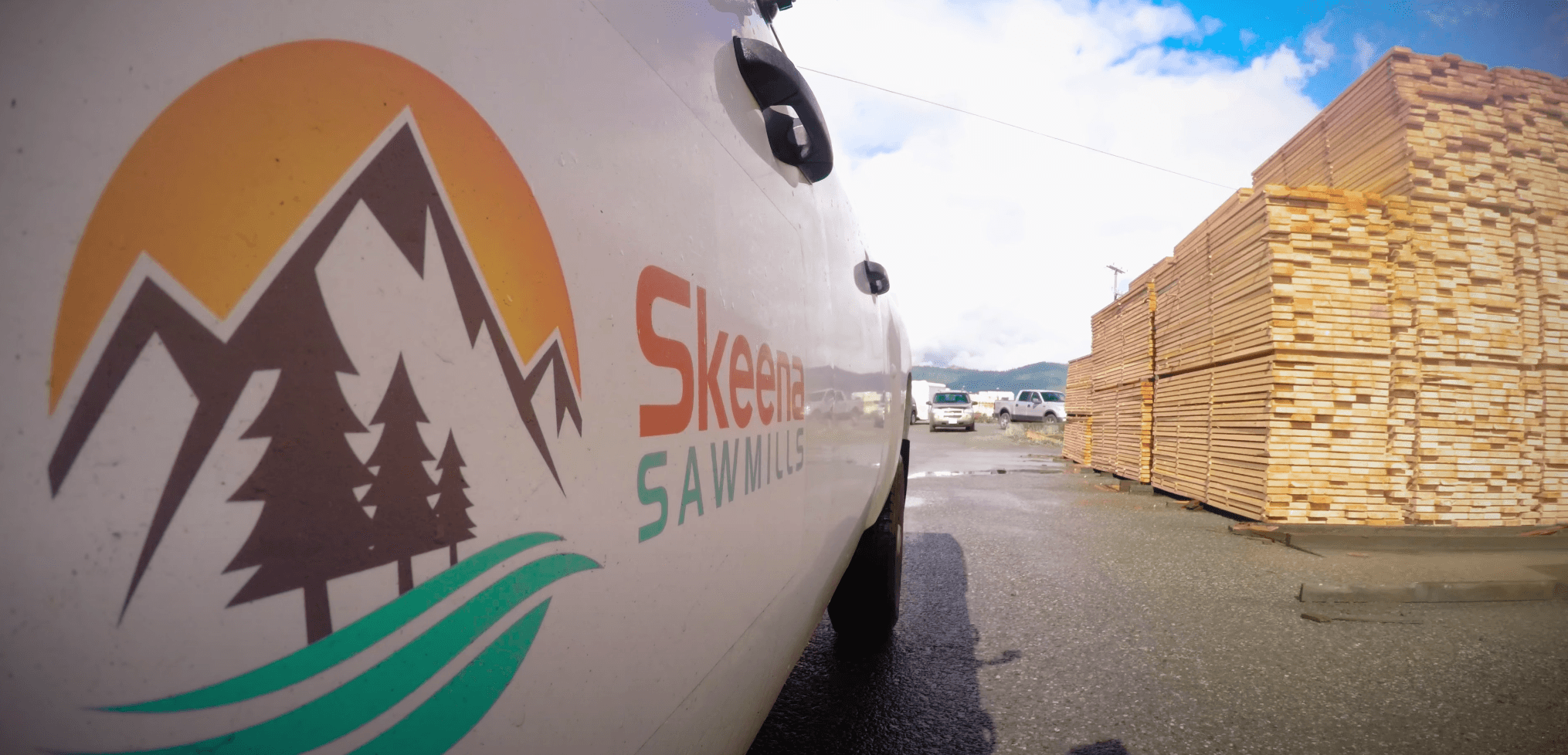 A white pickup truck with the Skeena Sawmills logo on the side drives through the mill's lumber yard.