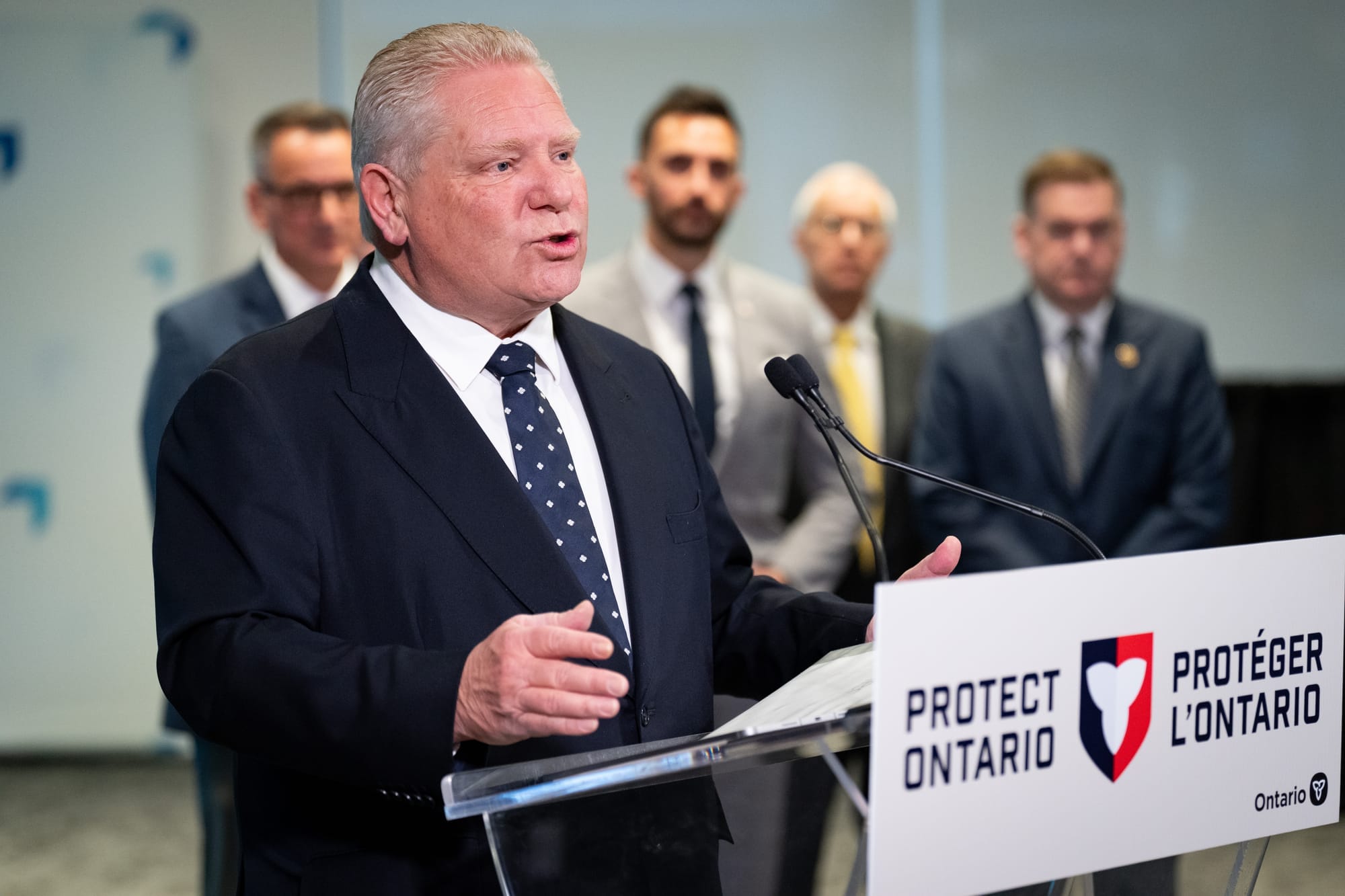 Doug Ford, wearing a suit and tie, speaks from behind a podium that says PROTECT ONTARIO.