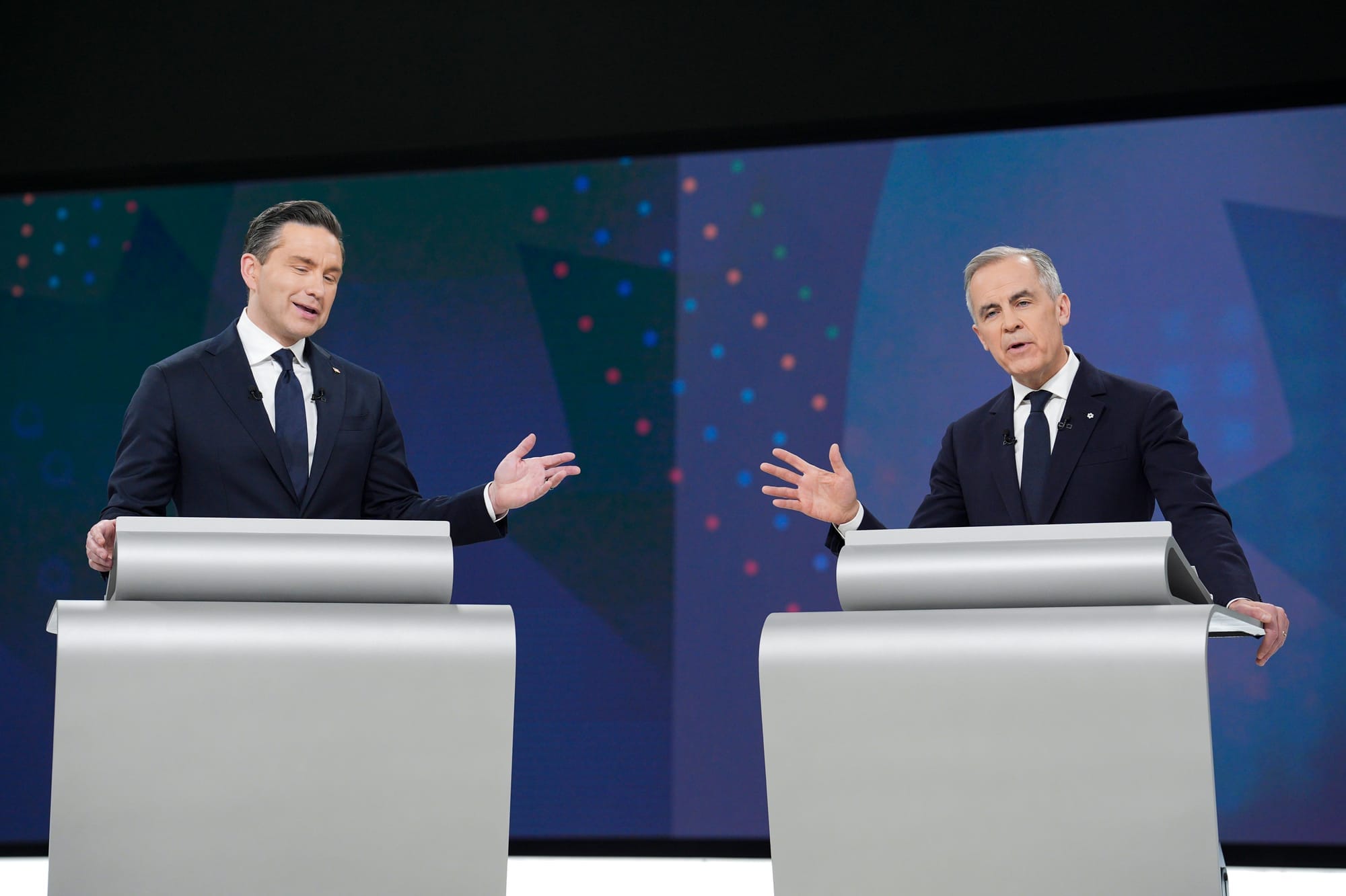 Pierre Poilievre stands behind a lectern and gestures with his left hand while Mark Careny makes a similar gesture with his left hand.