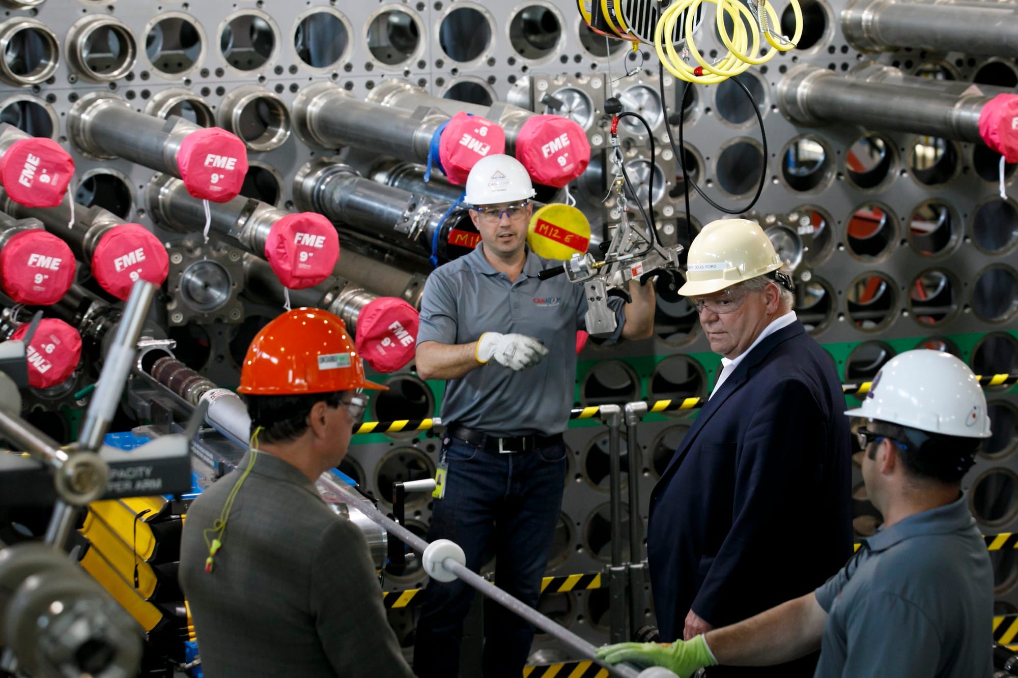 Doug Ford wears a hard hat while talking to workers surrounded by machinery at a nuclear plant. 