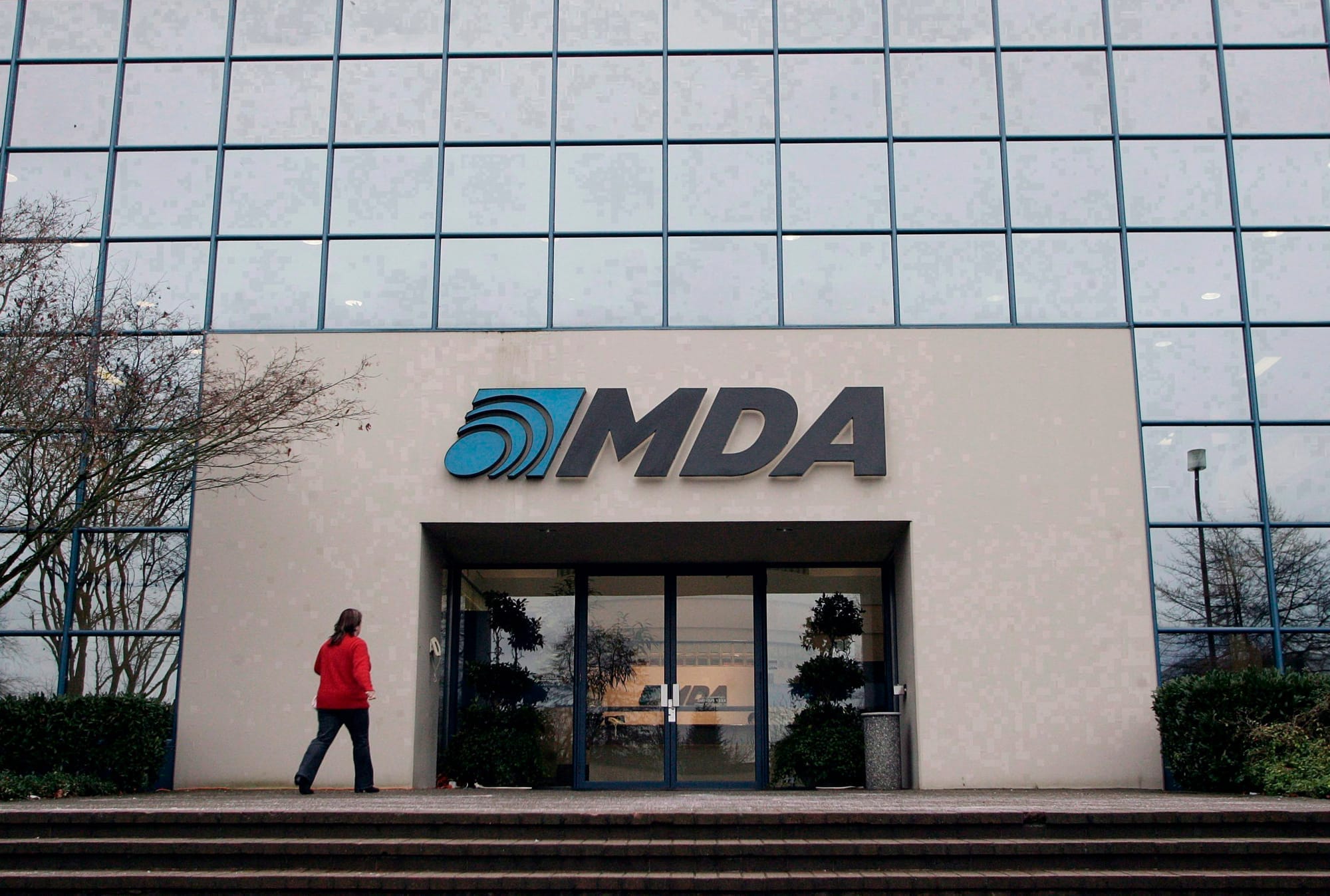 A woman wearing red walks toward the doors of a glass and concrete building with the a sign that says MDA.
