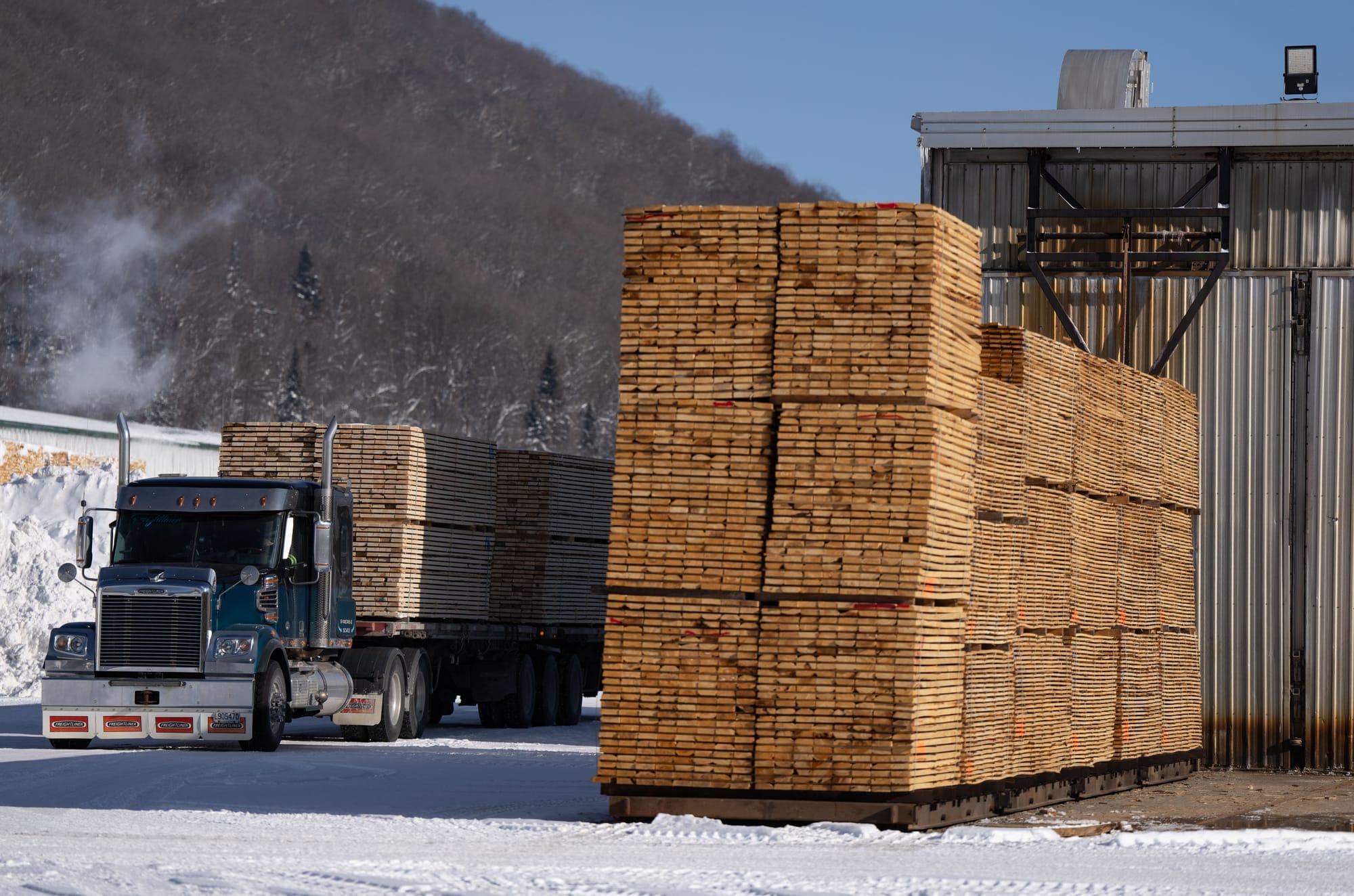 Stacks of wood are piled high in a lumber yard as a truck drives by 