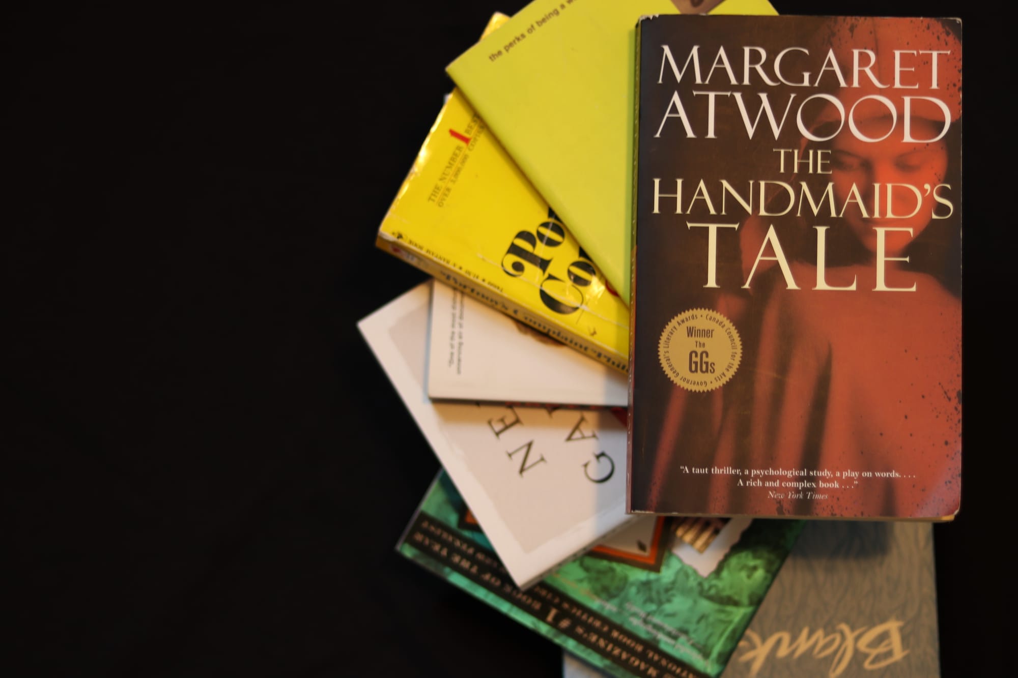 A stack of books with Margaret Atwood's The Handmaid's Tale in focus on top.