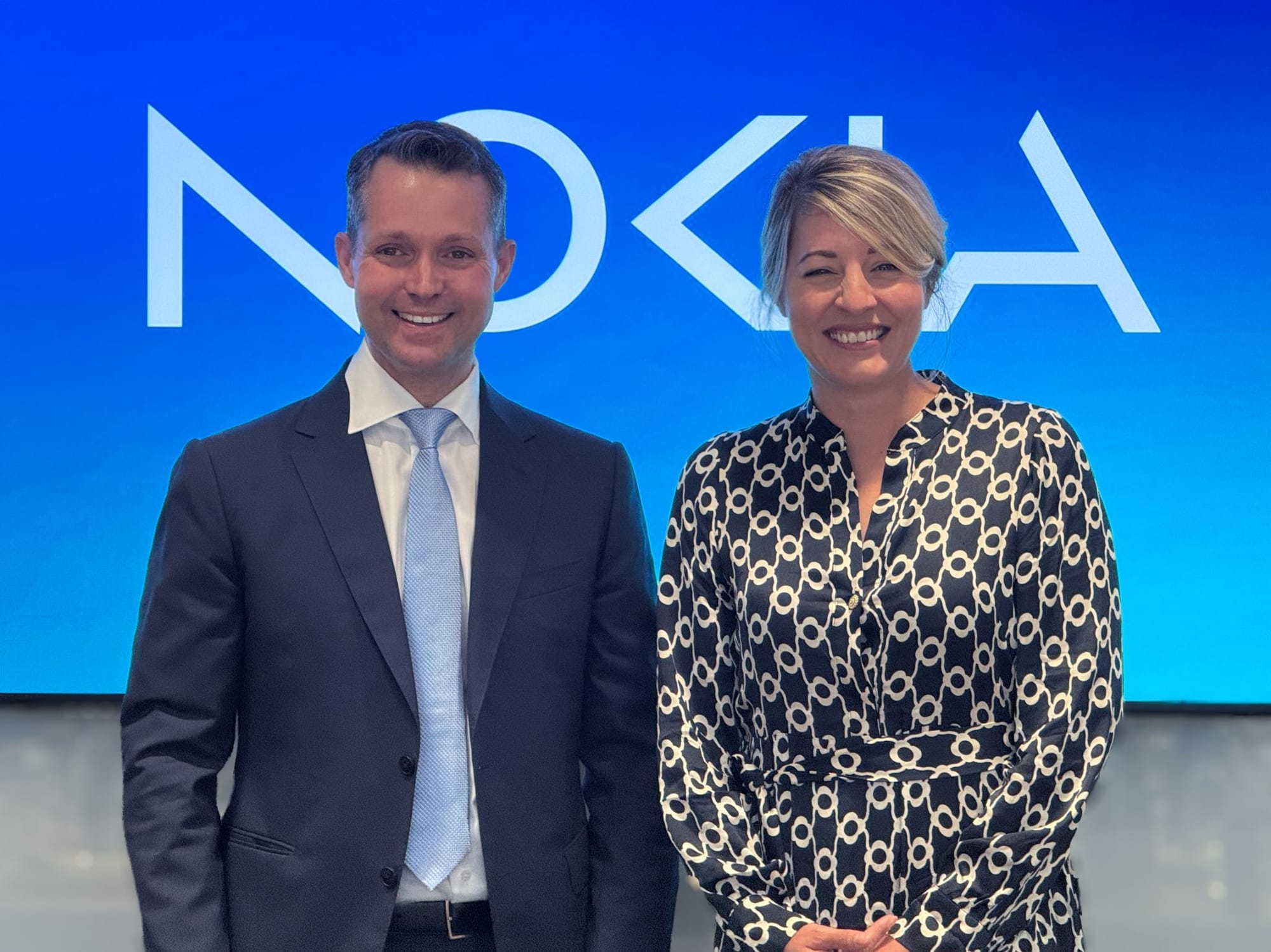 Justin Hotard wears a suit and stands next to Melanie Joly in front of a screen that says NOKIA