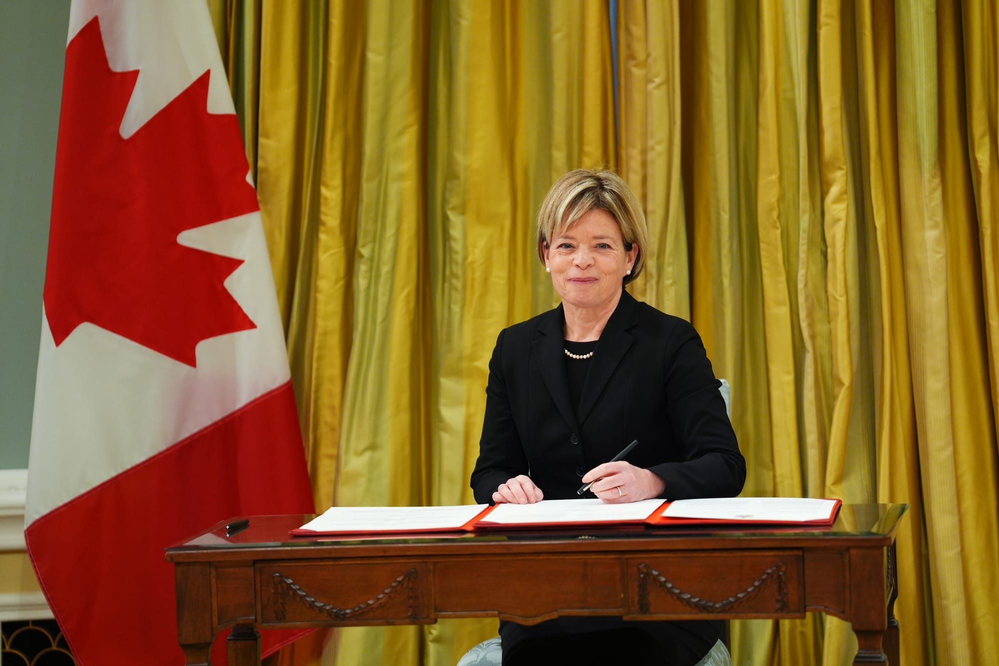 Former minister of national revenue Elisabeth Briere is seated and signs a document next to a Canadian flag at her swearing-in at Rideau Hall in Ottawa