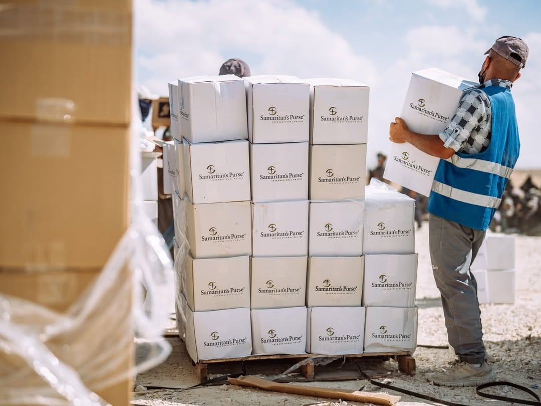A man in a blue vest loads boxes labelled "Samaritan's Purse" onto a pallet.