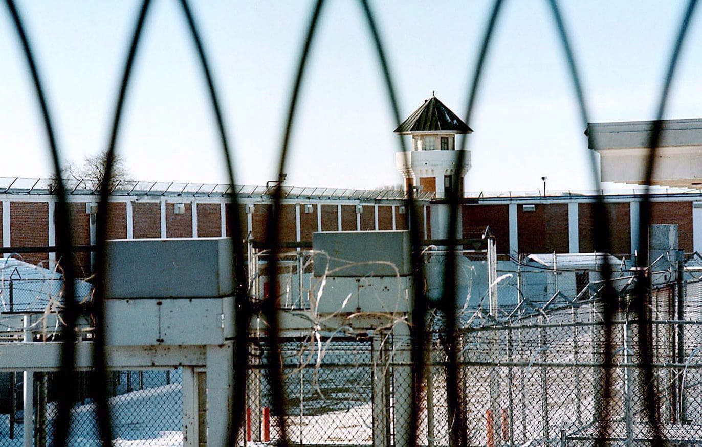 The yard of a Canadian prison is shown through concertina wire.