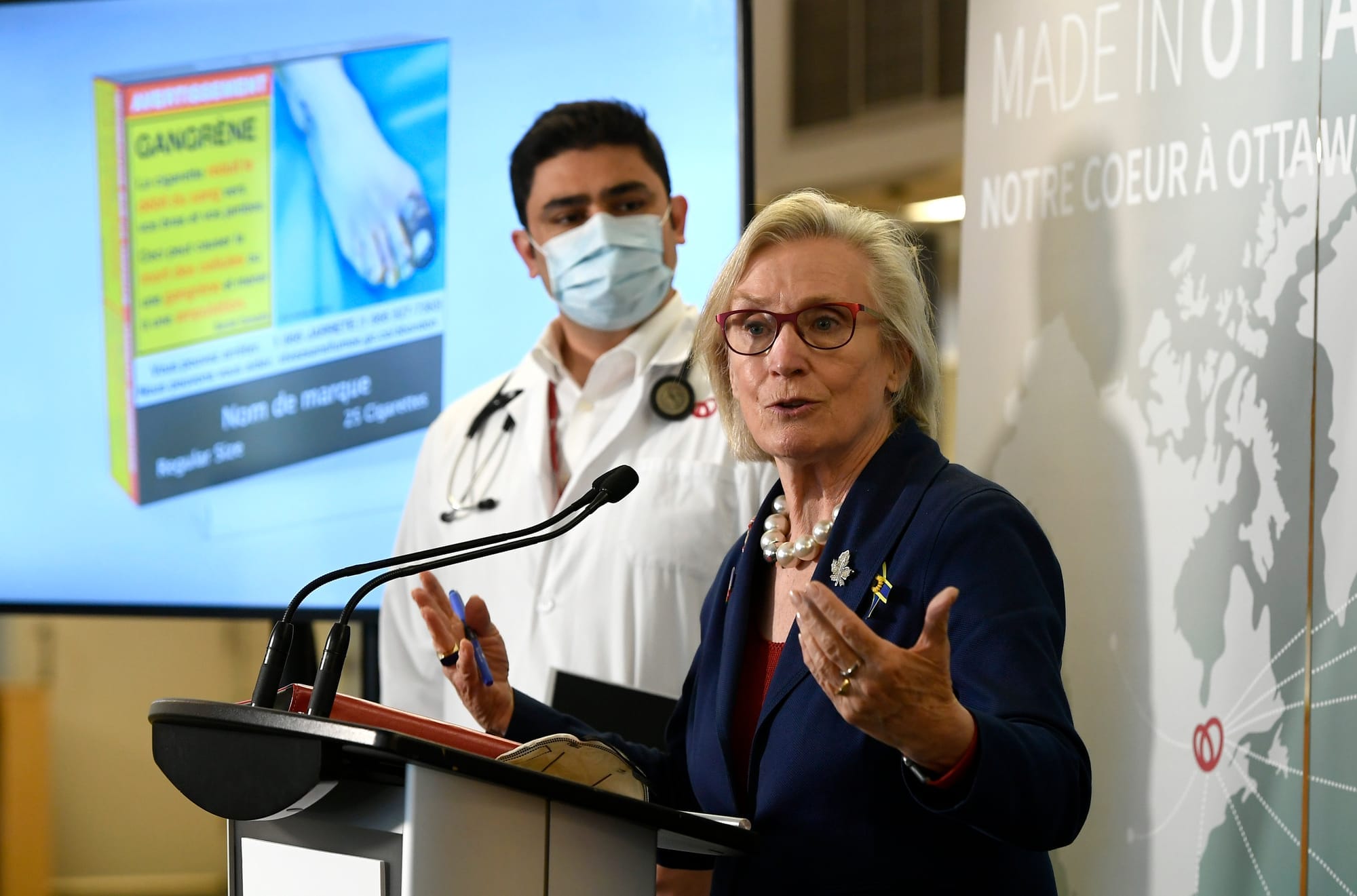 Former minister Carolyn Bennett and Dr. Hassan Mir, a University of Ottawa cardiologist, show an example of an updated cigarette package under federal rules.