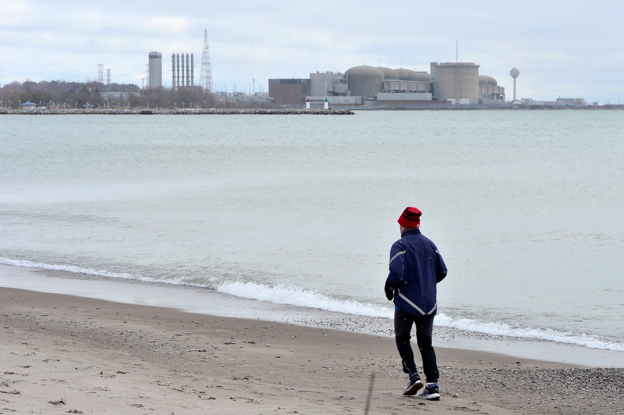 A jogger runs along the beach past the Pickering Nuclear Generating Station, in Pickering, Ont., in 2020.