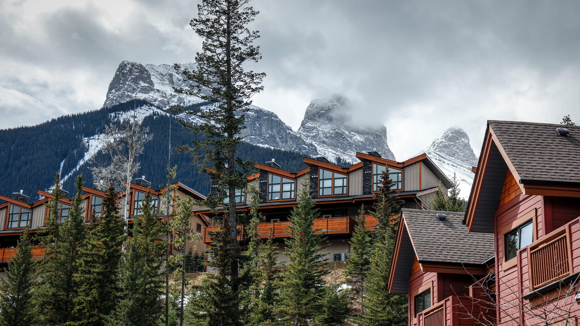 The peaks of the Three Sisters mountain range looms over homes hidden among pine trees in Canmore, Alta.