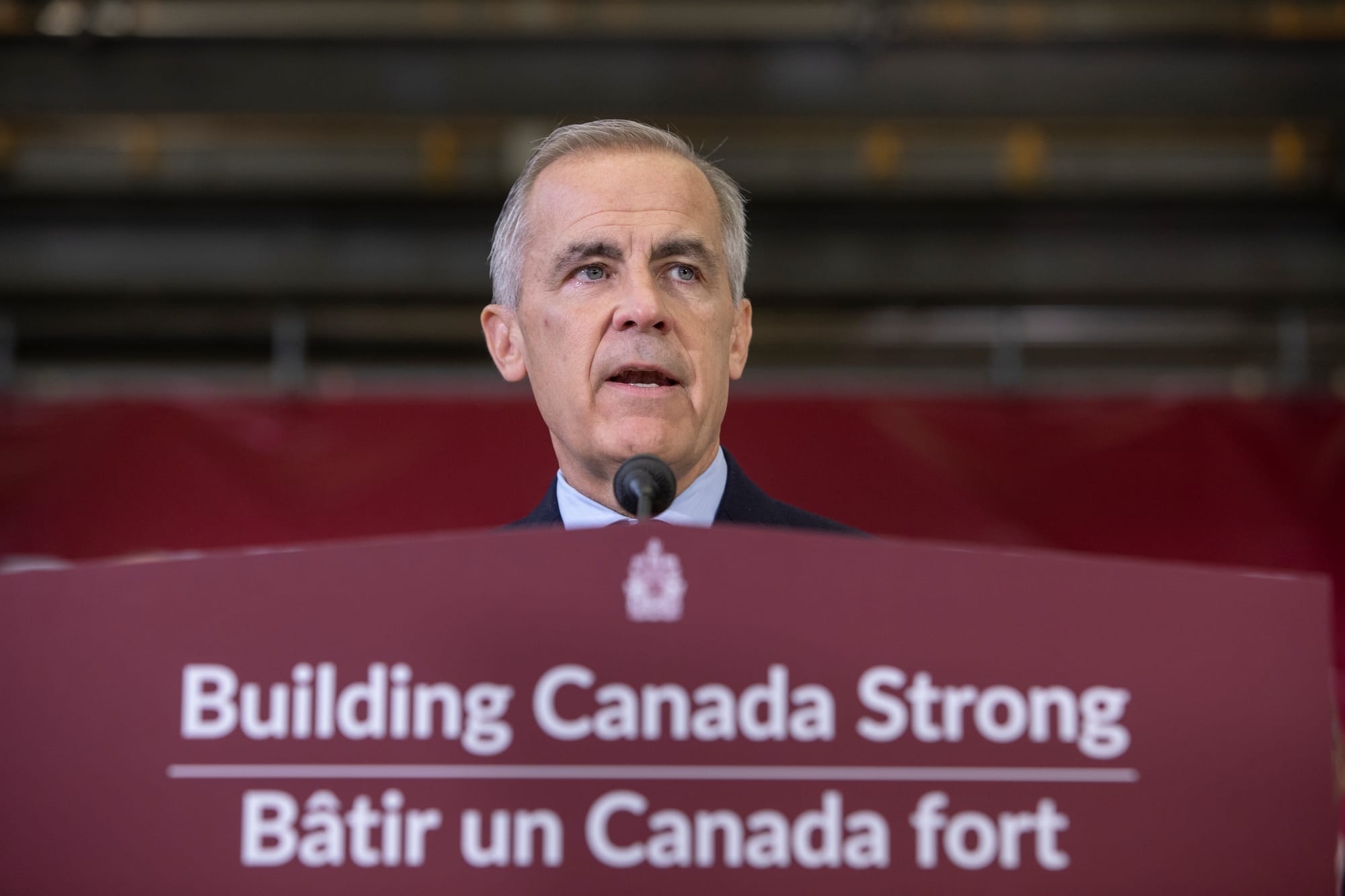 Prime Minister Mark Carney stands on a podium that has the phrase Building Canada Strong in English and French.