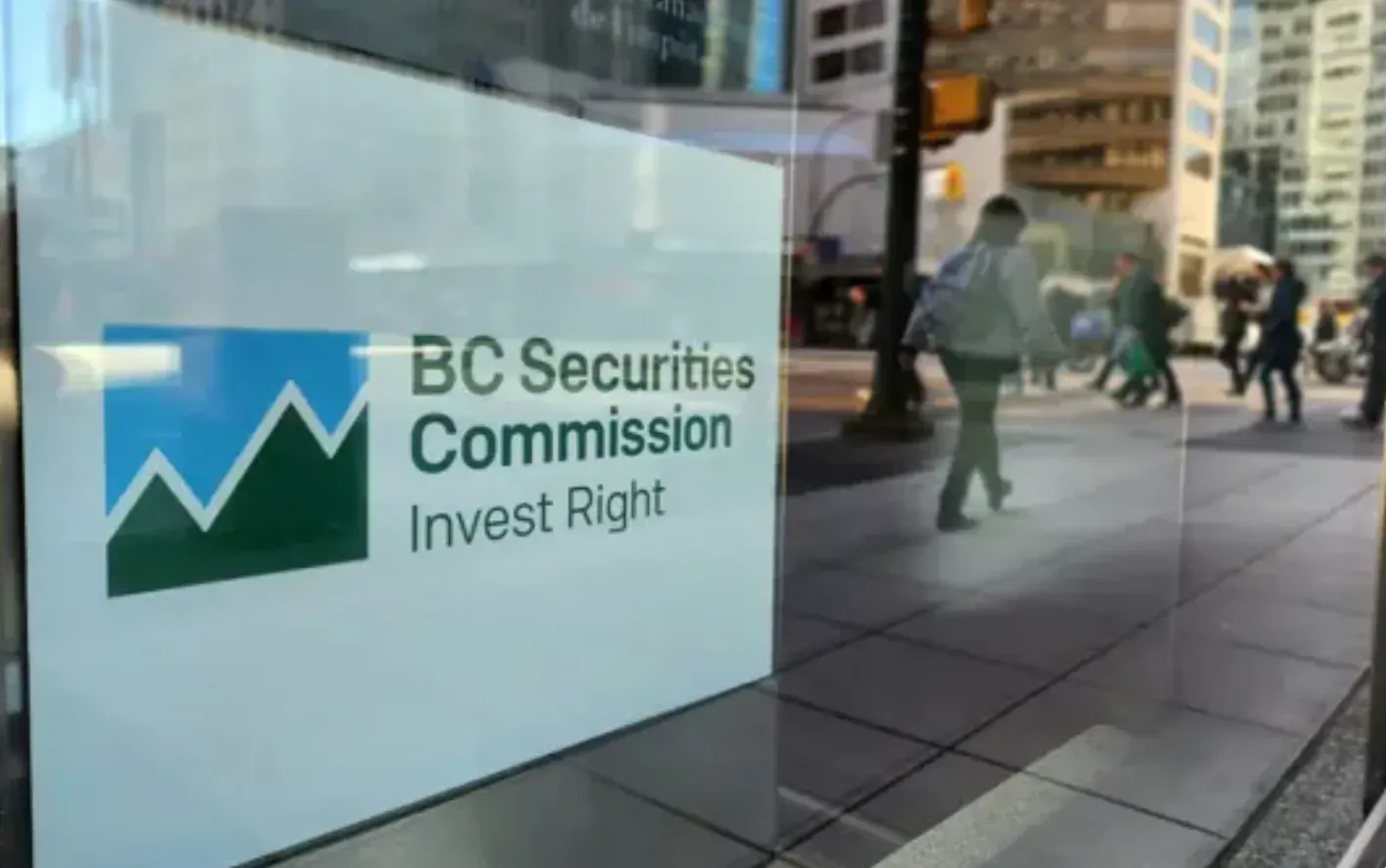 A white sign that says "BC Securities Commission: Invest Right" hangs behind a glass window on a downtown Vancouver street.
