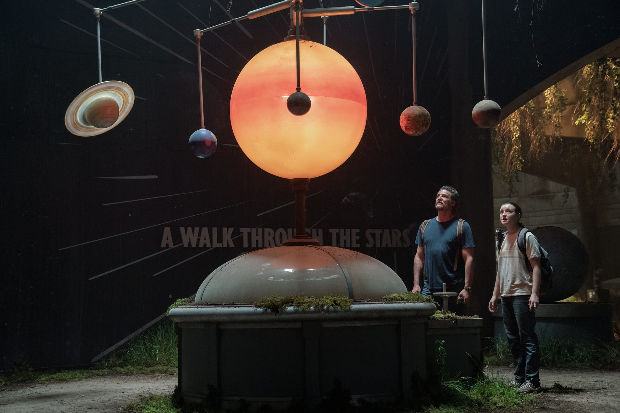 Two actors stare at a model of a solar system in an abandoned museum on the set of The Last of Us.