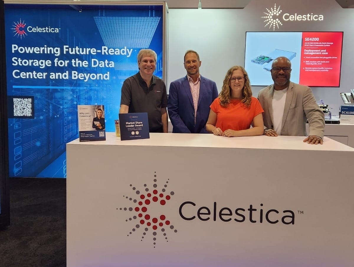Four Celestica representatives stand behind a display table that shows the company's name and logo.
